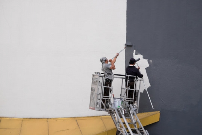 professionals painting the exterior of commercial building while standing in lift